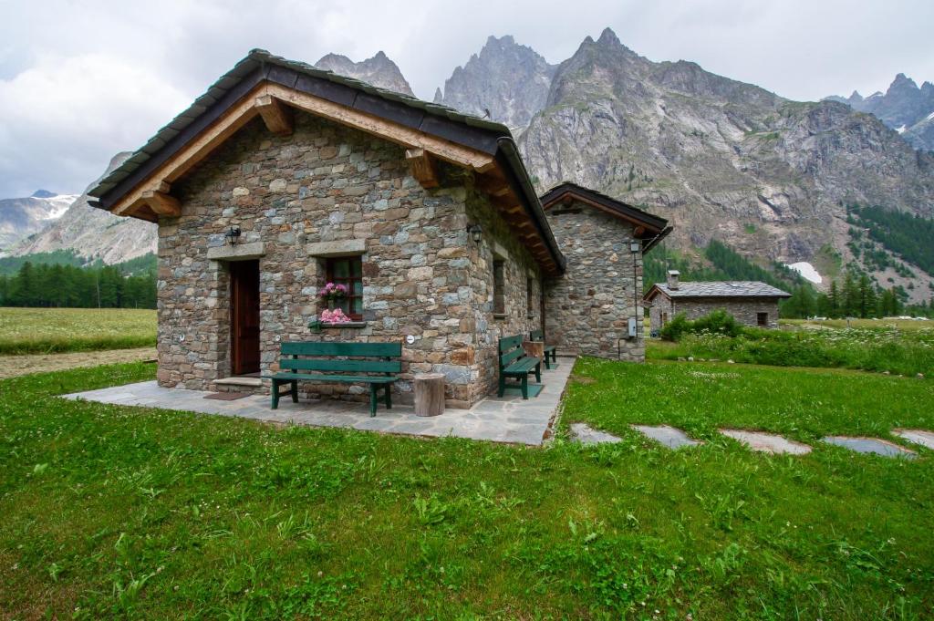 un piccolo edificio in pietra in un campo con montagne di Chalet Maison Felix a Pra Neiron
