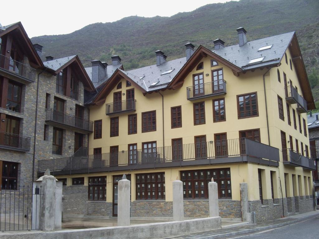 ein großes gelbes Gebäude mit einem Berg im Hintergrund in der Unterkunft Apartaments Pirinenc in Esterri d'Àneu