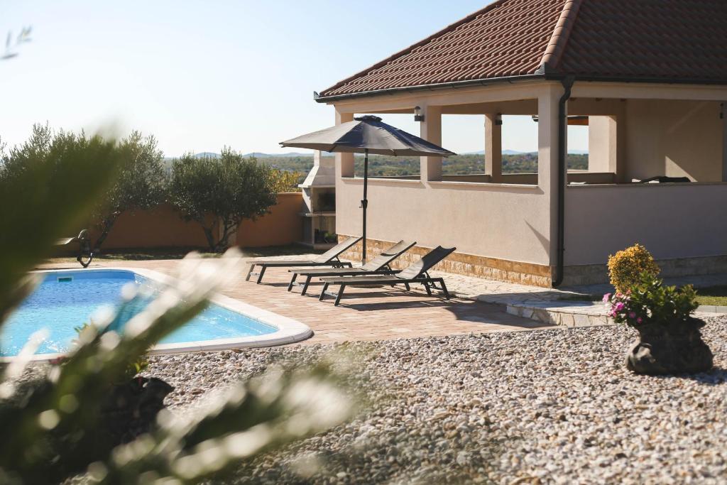 een huis met een zwembad en twee stoelen en een parasol bij Villa Zrilic ZadarVillas in Perušić Benkovački