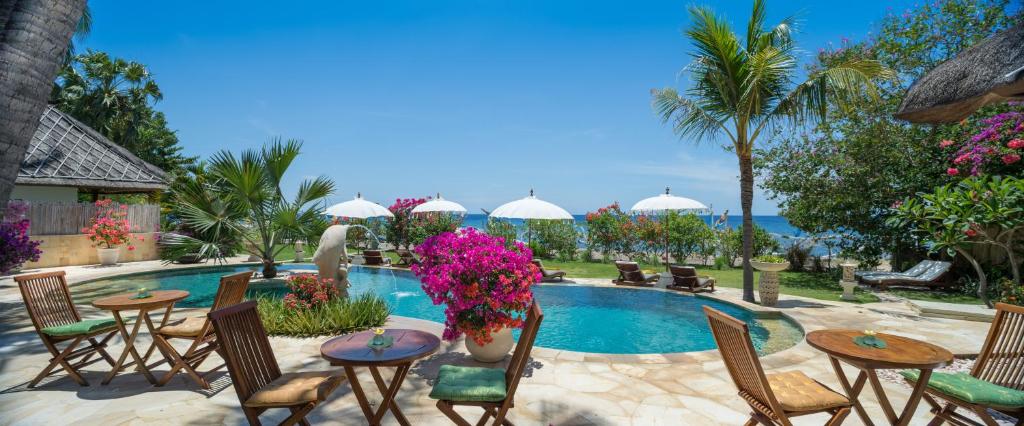 艾湄灣的住宿－巴厘島艾湄海灘棕櫚花園及Spa度假酒店，一座带桌椅和鲜花的游泳池