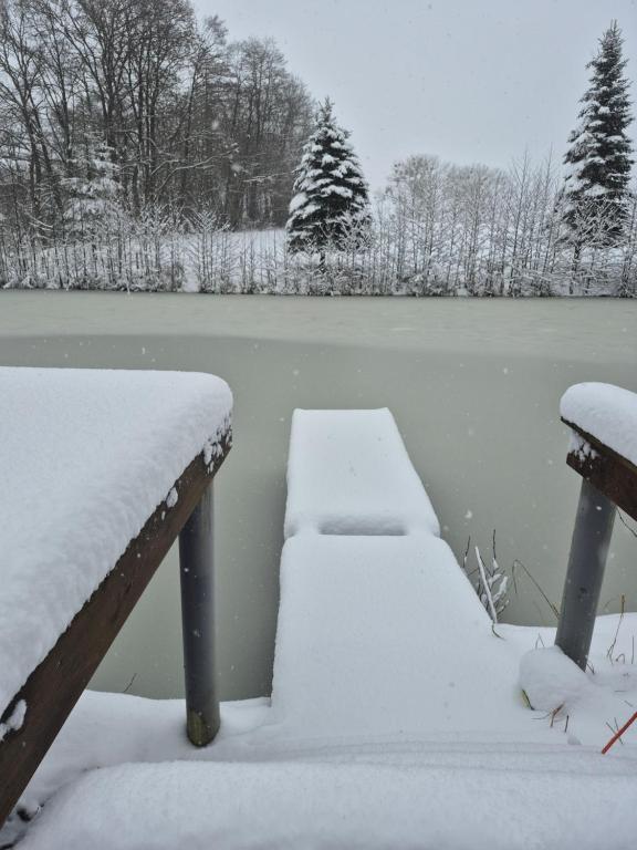 zwei schneebedeckte Bänke neben einem Gewässer in der Unterkunft Bliss Garden Retreat House ZielonoMi in Lengenquell