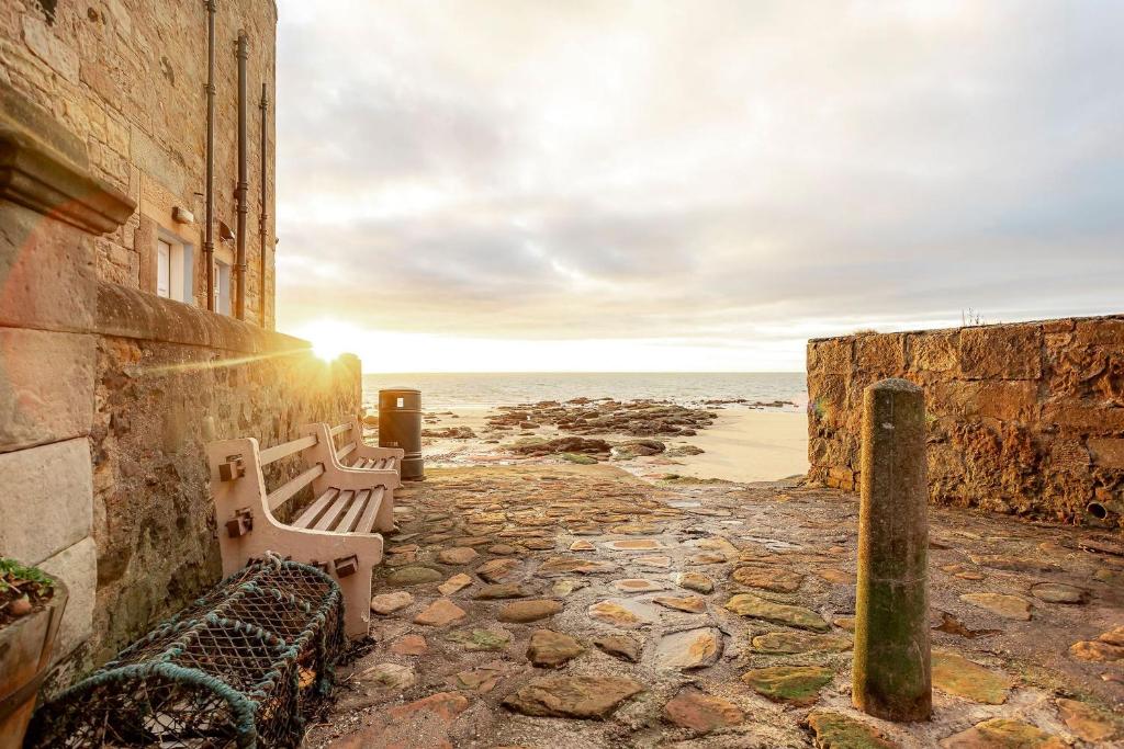 a bench sitting on the side of a building near the ocean at Main Street No 56 - Lower Largo in Lower Largo