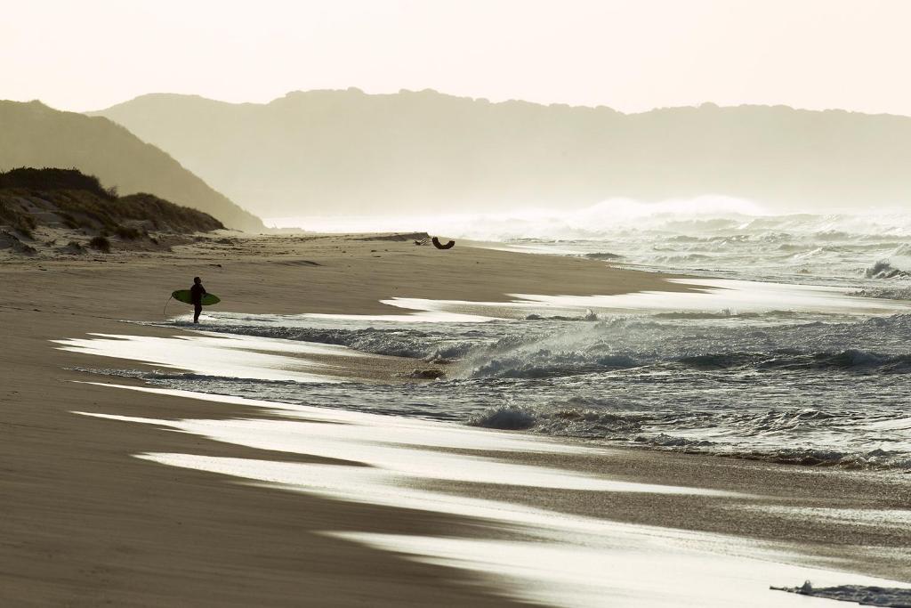una persona caminando por la playa con una tabla de surf en Island Breeze Motel en Currie