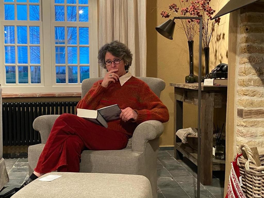 a woman sitting in a chair reading a book at Eikenbrand in Veurne
