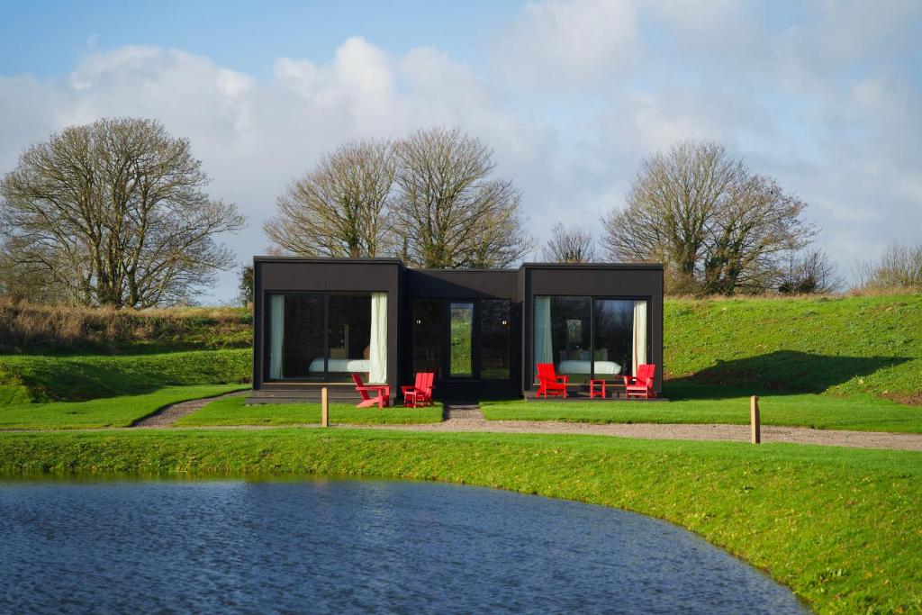 ein schwarzes Haus mit roten Stühlen und einem Teich in der Unterkunft Mad Swans in The Mendips in Farrington Gurney
