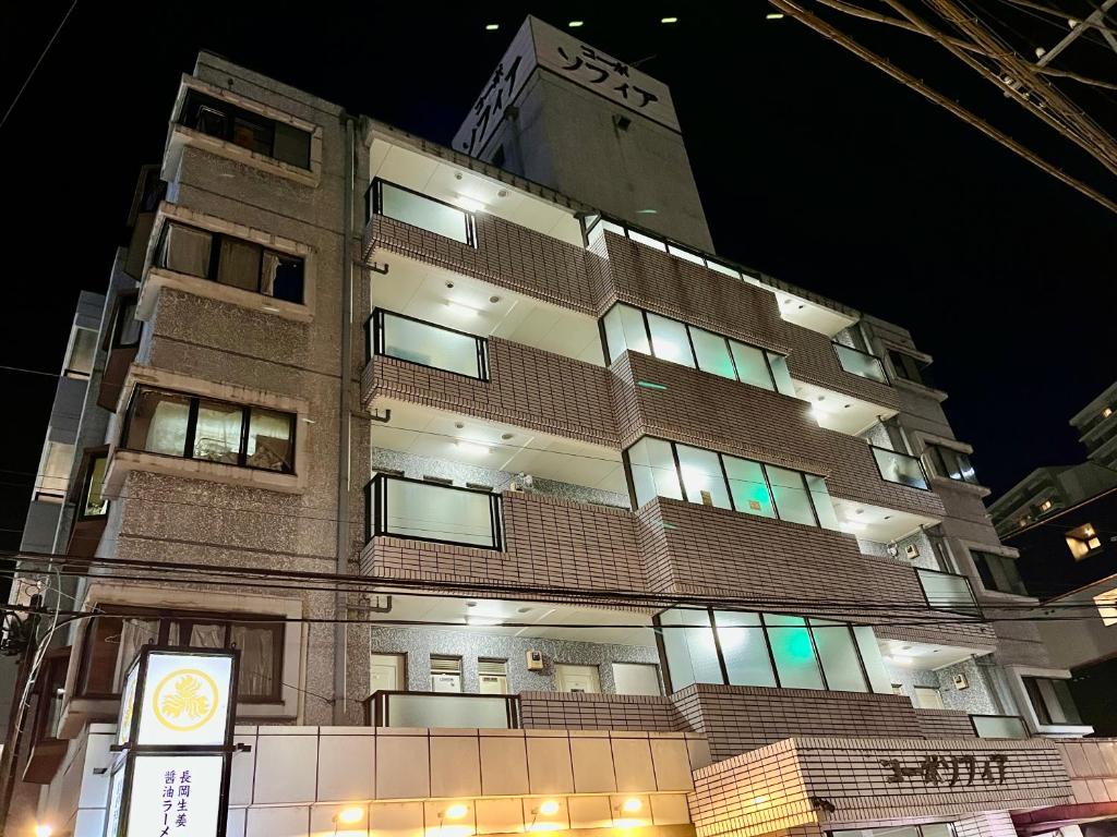 ein hohes Gebäude in der Nacht mit einem Schild davor in der Unterkunft Stay Plus Sophia in Utsunomiya