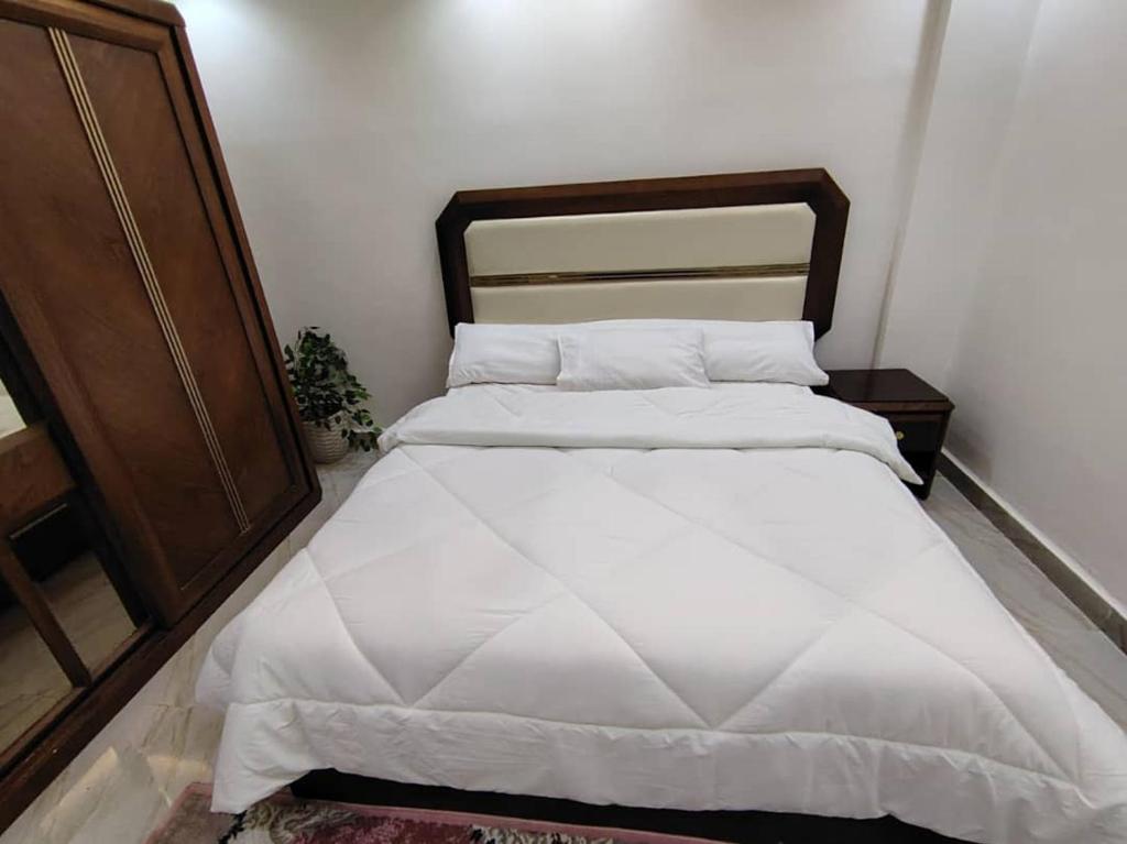 a bedroom with a large white bed with a wooden headboard at مدينتي in Kafr Salīm