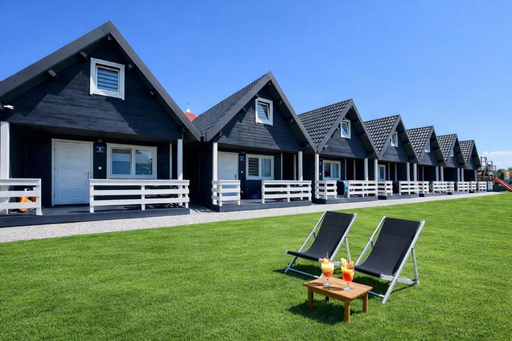 a row of houses with lawn chairs and drinks on a table at Domeczki Blaneczki Wicie - domki letniskowe nad morzem in Wicie