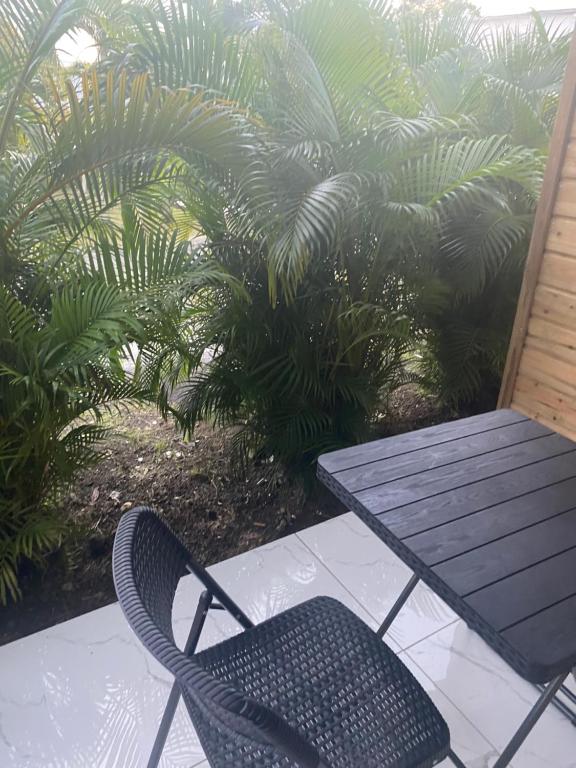 a table and a chair on a porch with palm trees at Bungalow cerise in Morne-à-lʼEau