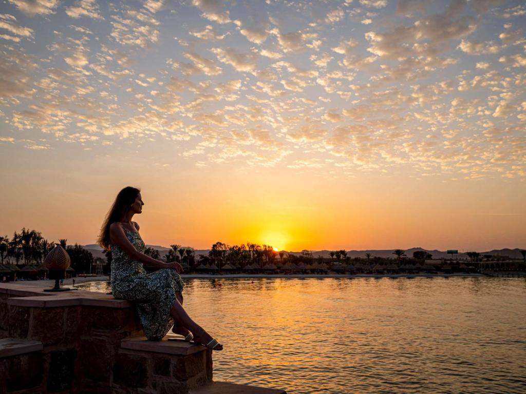 Eine Frau sitzt auf einem Pier und beobachtet den Sonnenuntergang. in der Unterkunft Movenpick Resort El Quseir in Al-Qusair