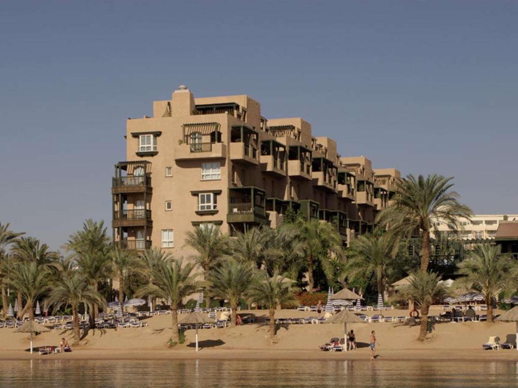 a large building on a beach with palm trees and people at Mövenpick Resort & Residences Aqaba in Aqaba