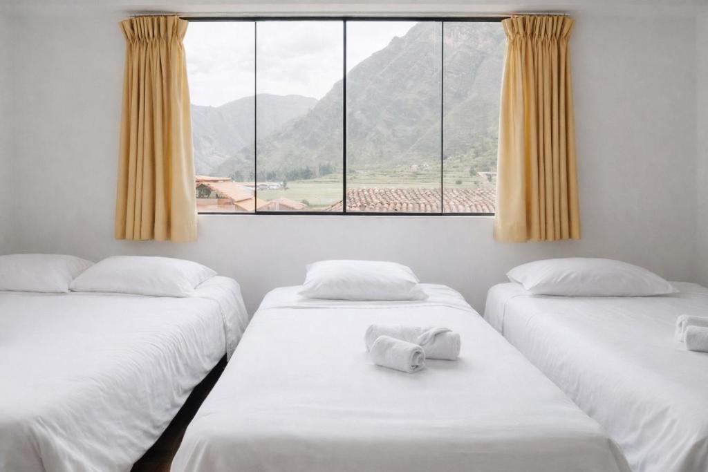 two beds in a room with a large window at Shanti Hotel Pisac in Pisac
