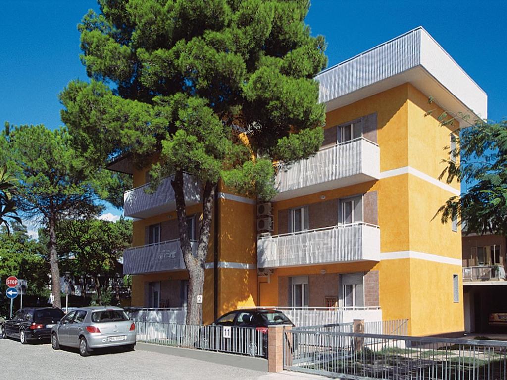 un edificio amarillo y blanco con coches estacionados frente a él en Patrizia, en Lignano Sabbiadoro