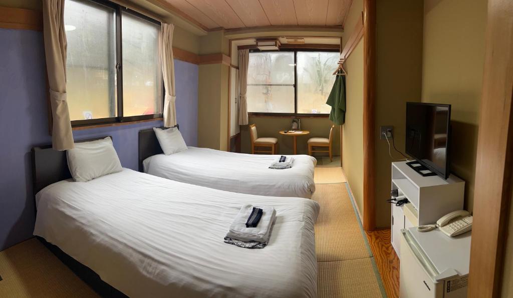 een kleine kamer met 2 bedden en een televisie bij ホテル富士山水館富士山一望河口湖車で3分HotelFujisanSuikanMtFujiView3 MinutesbyCartoLakeKawaguchi in Fujikawaguchiko
