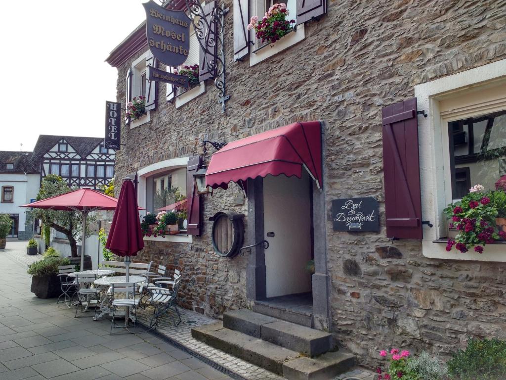 - un bâtiment en pierre avec des tables, des chaises et des parasols dans l'établissement Hotel garni Altes Winzerhaus Moselschänke, à Kobern-Gondorf