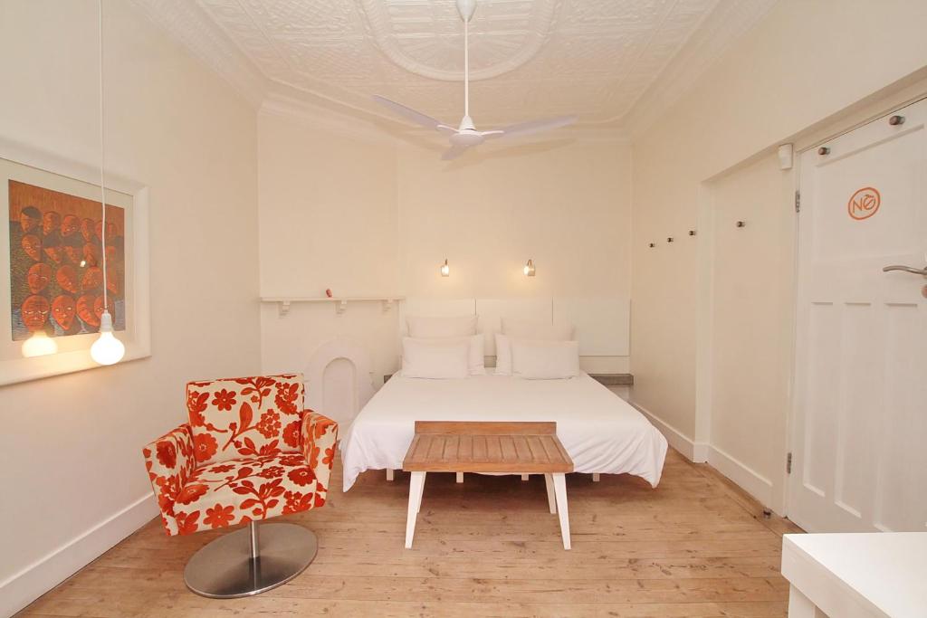 a white bedroom with a bed and a chair at Motel Mi Pi Chi in Johannesburg