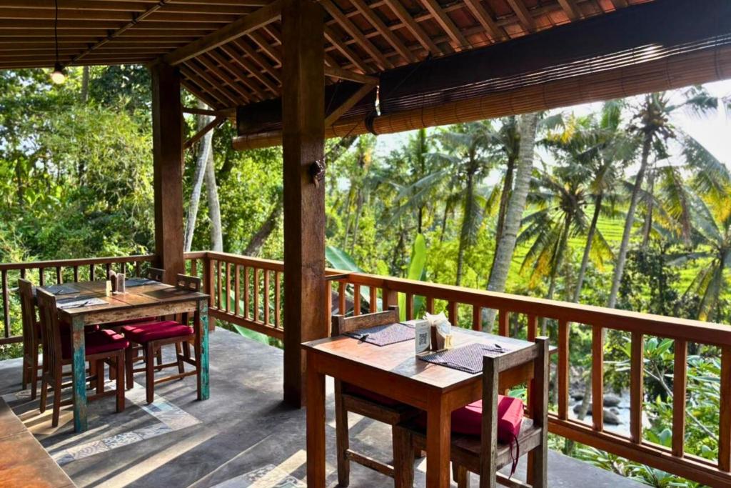 zwei Tische und Stühle auf einer Holzterrasse mit Bäumen in der Unterkunft Umasari Rice Terrace Villa by AGATA in Tabanan