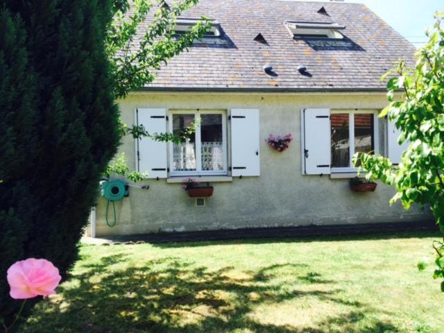 una casa con puertas blancas y flores en un patio en Le Clos Surcouf, en Isigny-sur-Mer