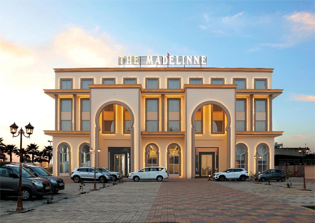 ein großes Gebäude, vor dem Autos parken in der Unterkunft The Madelinne Hotel in Muzaffarnagar