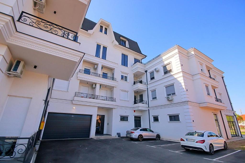 een groot wit gebouw met twee auto's geparkeerd op een parkeerplaats bij Apartman White Pearl in Palić