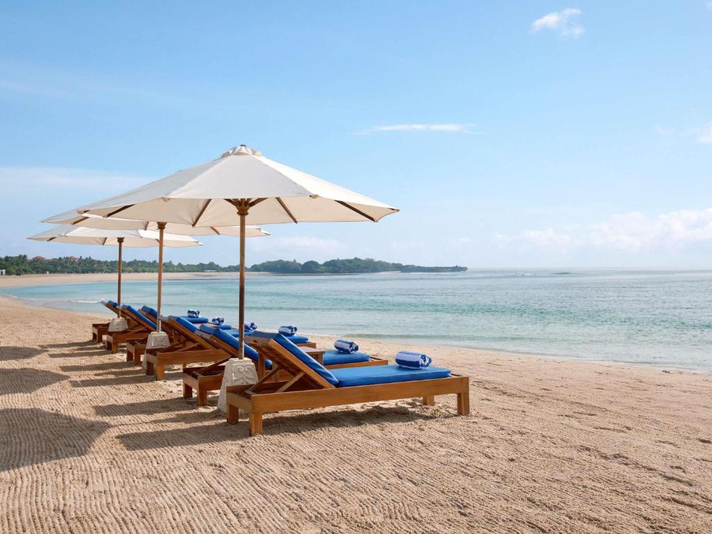 una fila di sedie a sdraio e ombrelloni in spiaggia di Novotel Bali Nusa Dua a Nusa Dua