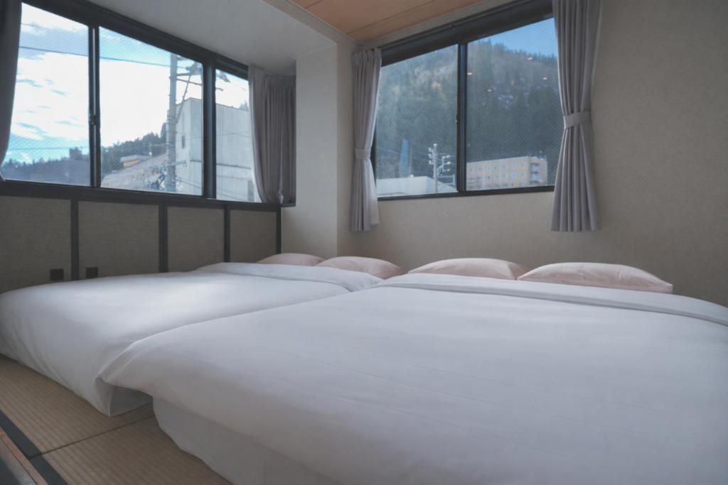 een wit bed in een kamer met 2 ramen bij AURA YUZAWA Apartment Hotel - 1Bedroom Apartment with Living Dining Kitchen Sleeps 2 to 4, Bedroom with 2-Double Bed, Living Room with 1-Sofa Bed in Yuzawa