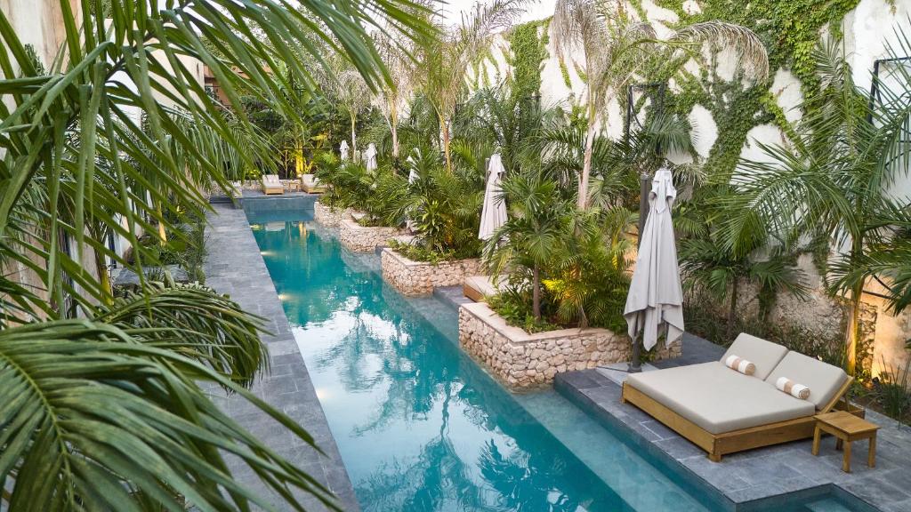 een overloopzwembad met een ligstoel, parasol en palmbomen bij Ontico Urban Design Hotel in Mérida