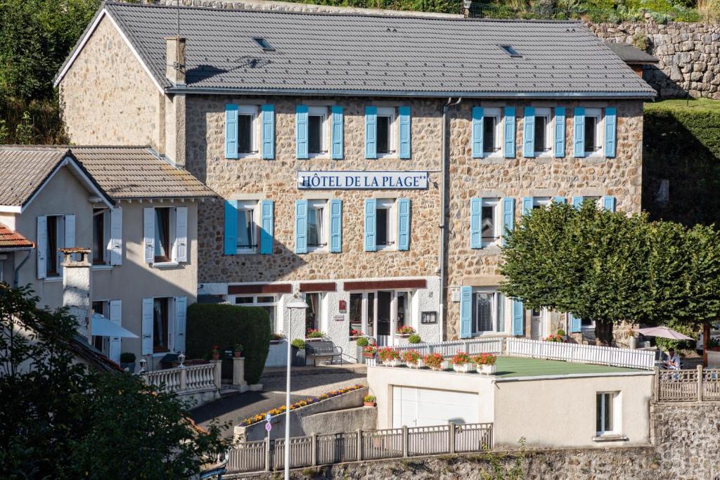 un grand bâtiment en briques avec des volets bleus dans l'établissement Hôtel De La Plage, au Chambon-sur-Lignon