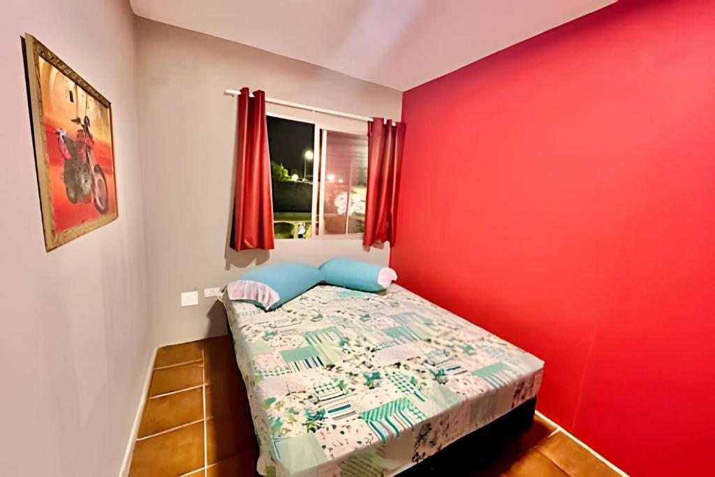 una piccola camera con una parete rossa e un letto di The Red, Vem que tem Sol a Matinhos