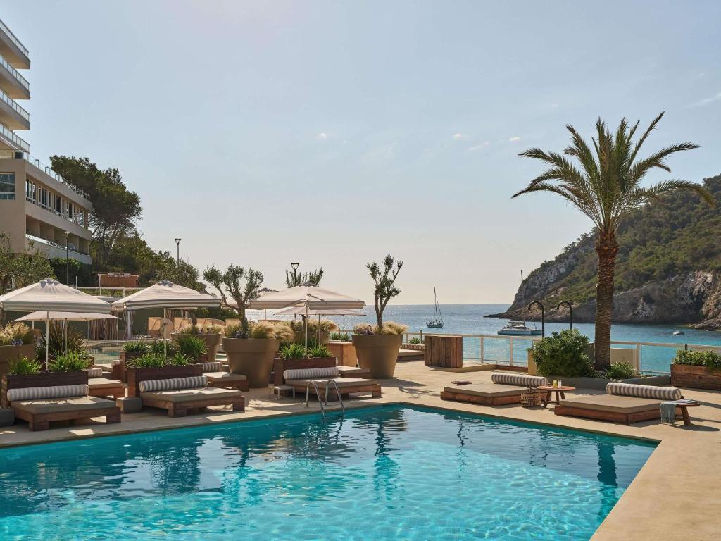 una piscina con sedie a sdraio e l'oceano di Mondrian Ibiza a Cala Llonga