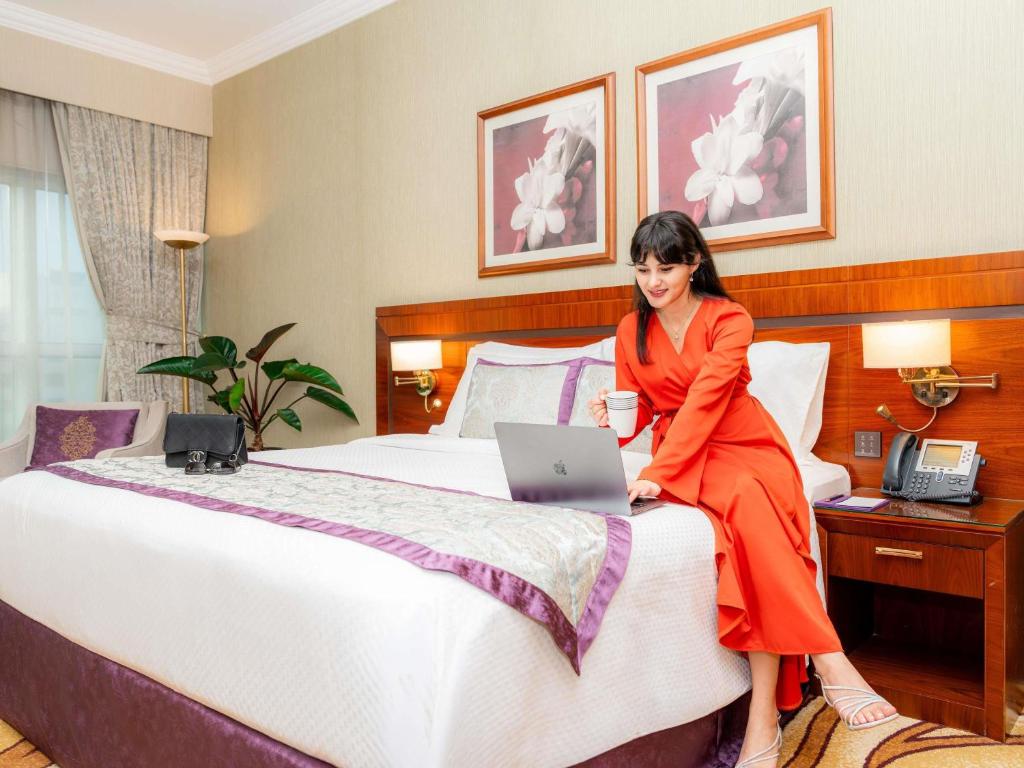 een vrouw op een bed met een laptop bij Grand Mercure Majlis Residences Abu Dhabi in Abu Dhabi