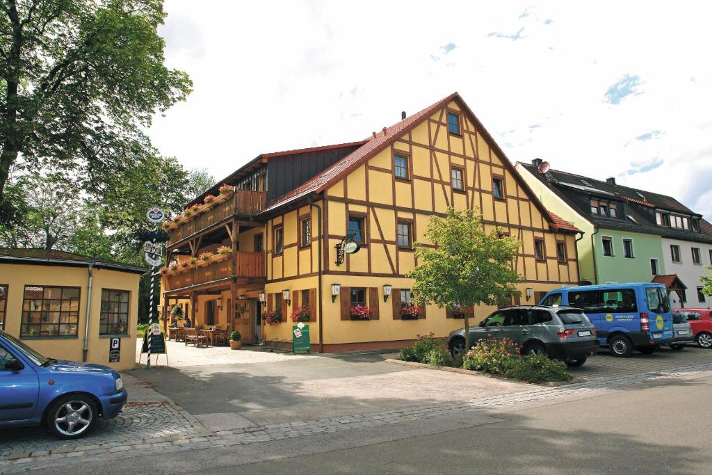 un grand bâtiment jaune avec des voitures garées dans un parking dans l'établissement Gasthof Schönau, à Heilsbronn