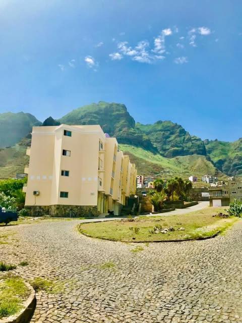 a street with a building and mountains in the background at Ritmo Turístico in Ponta do Sol