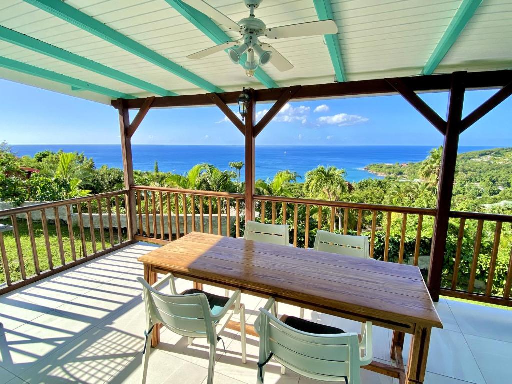 einen Holztisch und Stühle auf einem Balkon mit Meerblick in der Unterkunft Espace Harmonie Deshaies - Vue Mer & Piscine Panoramique in Deshaies