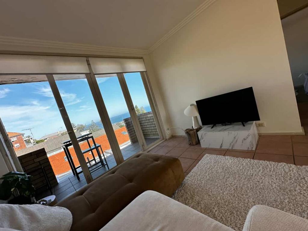 een woonkamer met een bank en een flatscreen-tv bij Beach & Ocean View Apartments Tamarama in Sydney