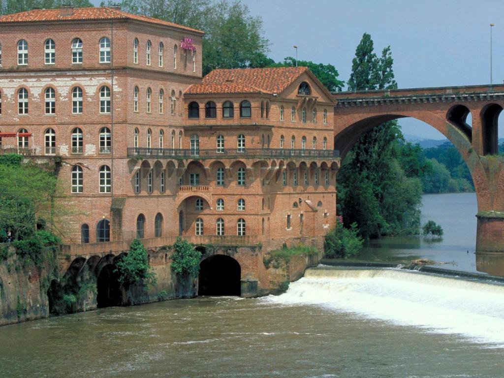 een brug over een rivier met een groot bakstenen gebouw bij Mercure Albi Rives du Tarn in Albi