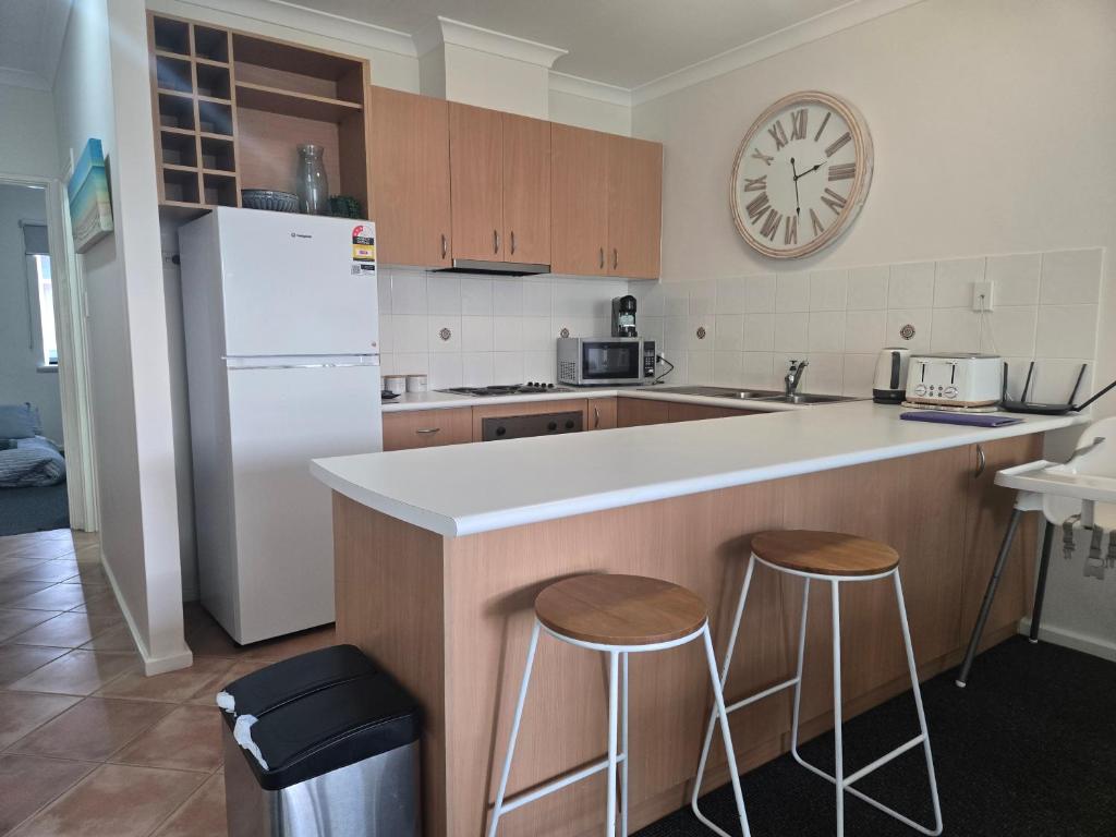 a kitchen with a white refrigerator and two bar stools at Waterfront Hideaway with Pool, Spa & BBQ Area jetty available in Mandurah