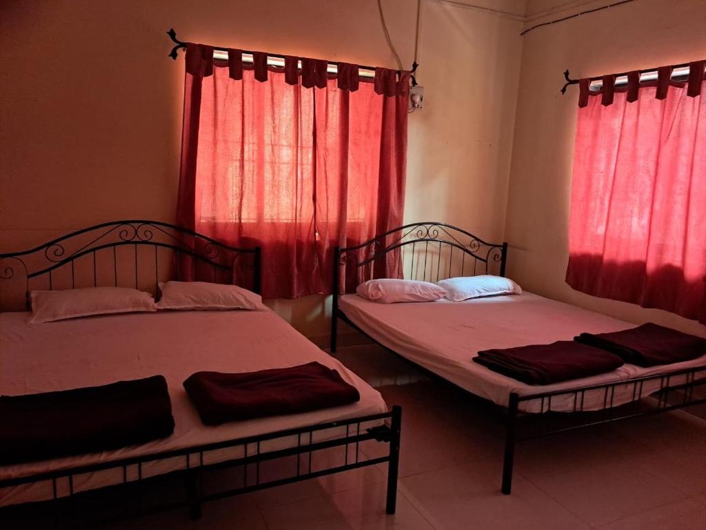 two beds in a room with red curtains at Hotel Cosy Nook in Malvan