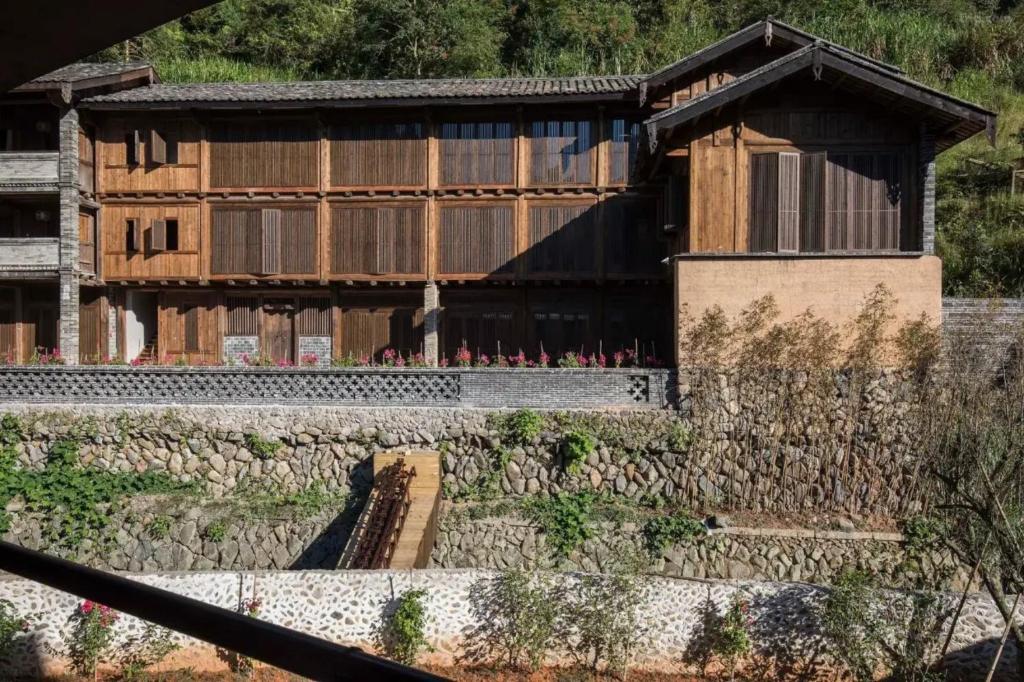 een gebouw met een stenen muur ervoor bij Tsingpu Tulou Retreat 青普文化行馆 南靖土楼店 in Nanjing