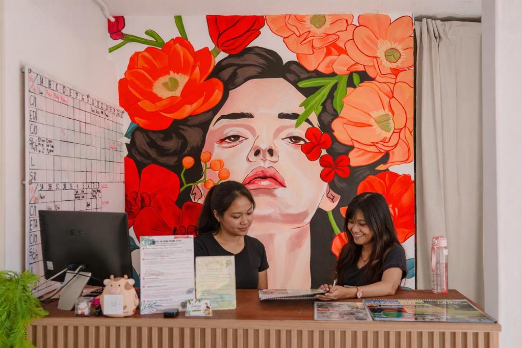 Twee vrouwen zitten aan een bureau voor een grote muurschildering van bloemen. bij Snooze Malang in Malang
