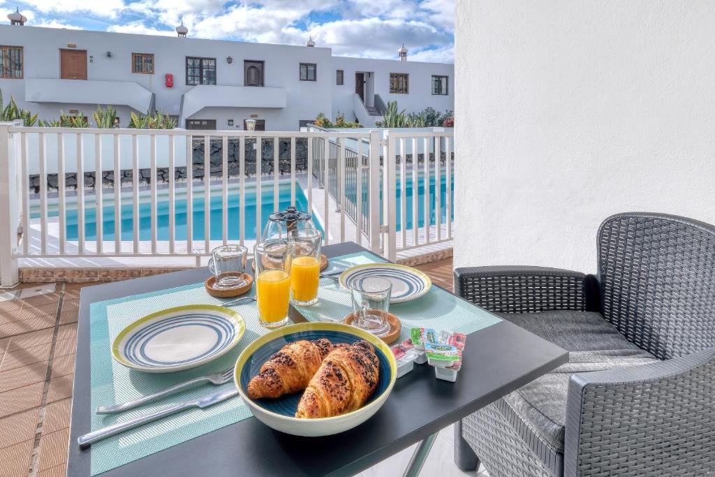 a table with a breakfast of croissants and orange juice at Carpe Diem Apartment - Pool view By Lanzarote Vacation Homes in Puerto del Carmen