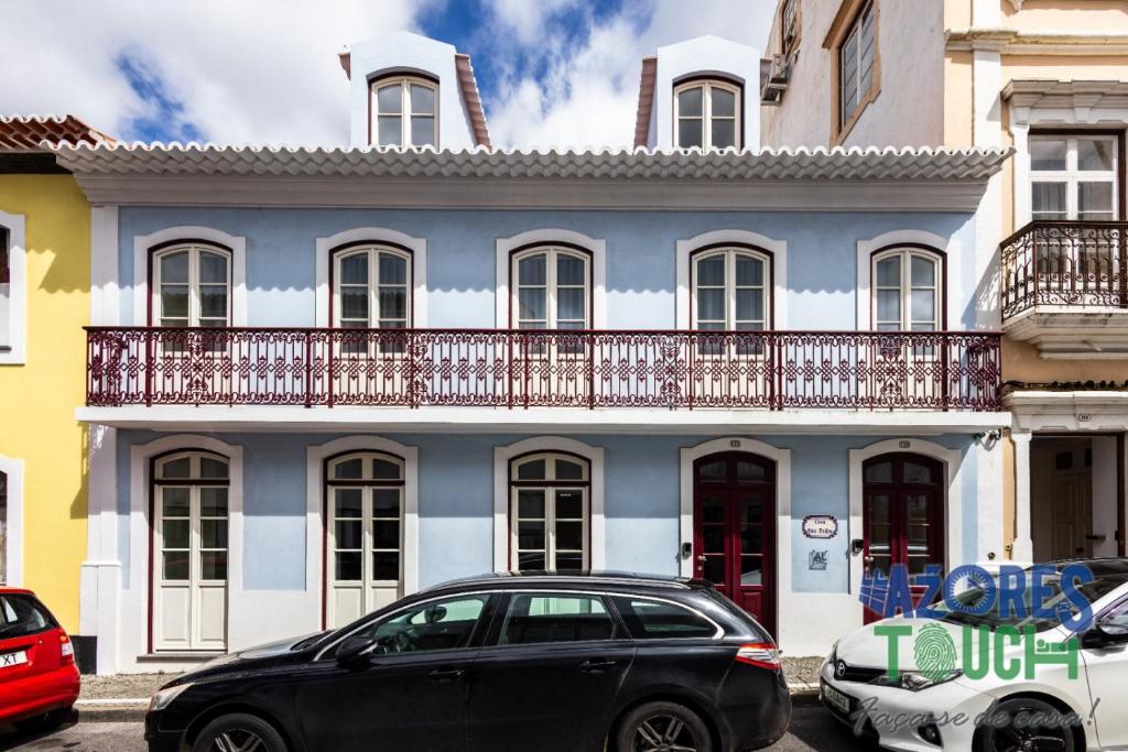 ein schwarzes Auto, das vor einem blauen und weißen Gebäude parkt in der Unterkunft Hostel Casa São Pedro in Angra do Heroísmo