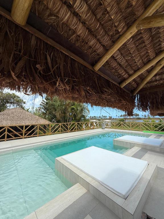 an outdoor swimming pool with a thatched roof at Pousada Vila Bacana in São Miguel do Gostoso