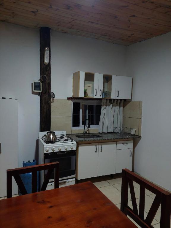 une cuisine avec des armoires blanches, une cuisinière et une table dans l'établissement Canaña Los Comechingones, à Santa Rosa de Calamuchita