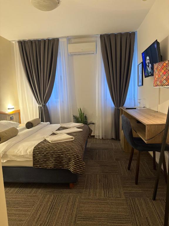 a bedroom with a bed and a desk and curtains at Hotel Previla in Sarajevo