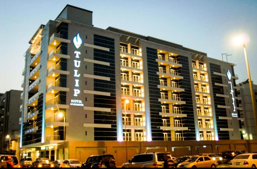 duży budynek z samochodami zaparkowanymi przed nim w obiekcie Tulip Hotel Apartments w Dubaju