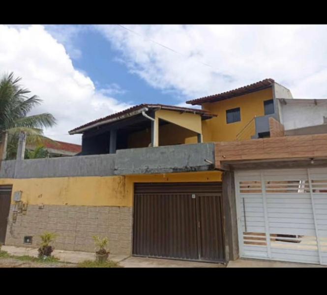 a yellow house with two garage doors and a palm tree at Casa para Reveillon - cururupe in Ilhéus