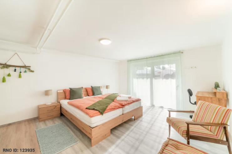 a white bedroom with a bed and a chair at Bah Apartment in Ljubljana