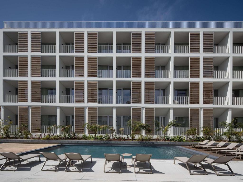 an external view of a hotel with chairs and a swimming pool at Mercure Ponta Delgada Azores in Ponta Delgada