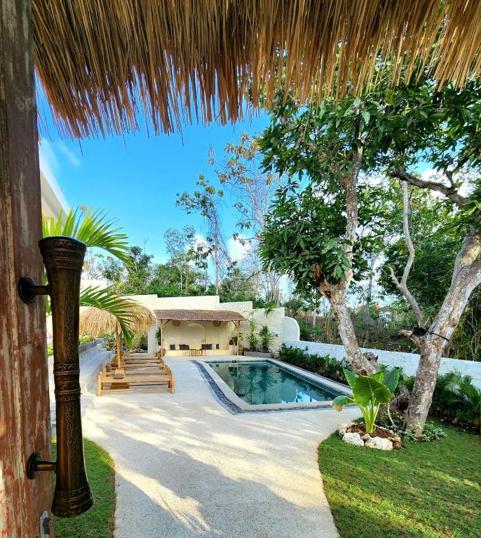 a backyard with a swimming pool and a straw roof at Villa Solara in Uluwatu